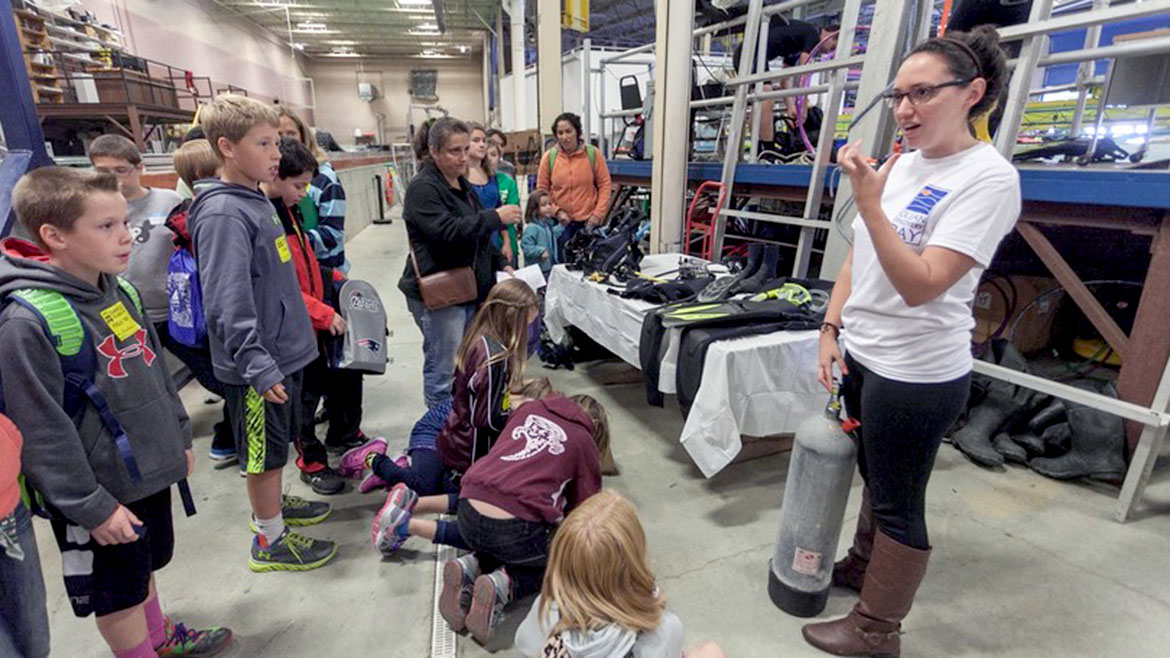 Volunteer speaking with students by tank. 