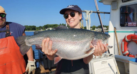 Photo of woman holding a large steelhead trout on a boat at sea. 