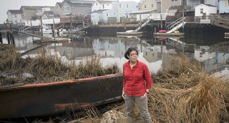 Helen standing by the shore with row of houses in background.