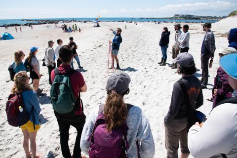 Group of students gathered around leader on beach.