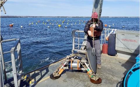 Color photo of man deploying instrument from boat. 