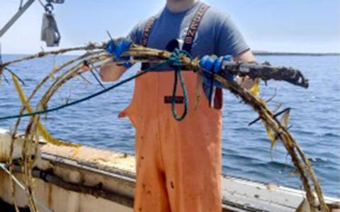 Person on boat in orange waders holding large ring. 