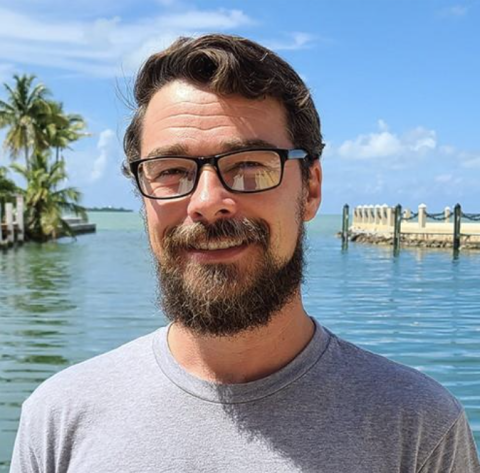 Photo of man standing in front of ocean on sunny day.