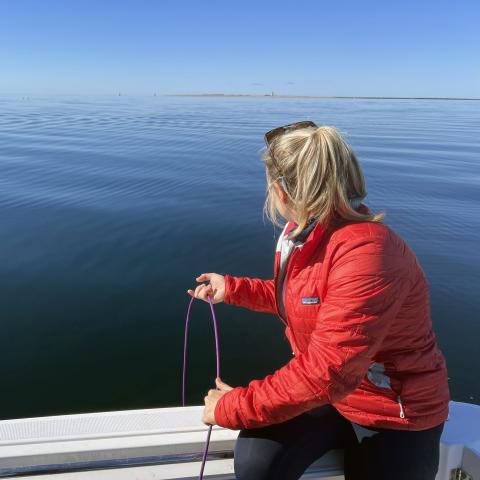 Image of student sitting on the side of a boat dropping a line into the ocean. 
