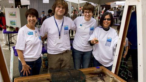 Four smiling volunteers in ODD shirts by the touch tank. 