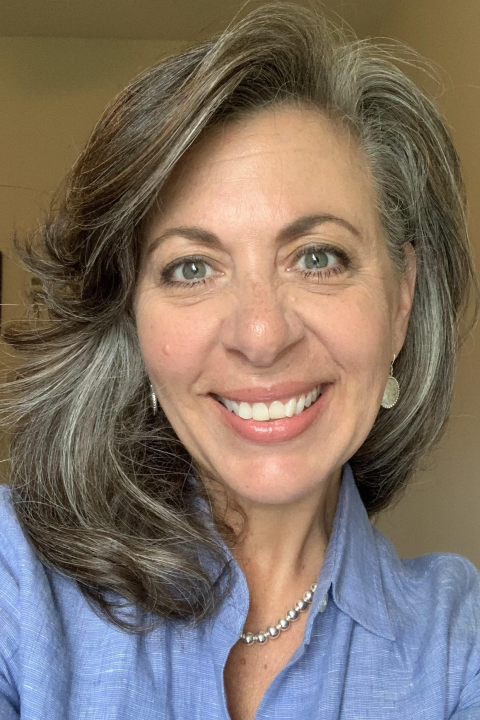 Amy Fish, a white woman with shoulder length brown hair with some gray and gray eyes in a light blue collared shirt. She smiles at the camera.